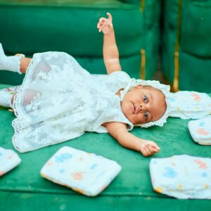 Cute baby in a white dress playing on a green sofa with diapers nearby. Ideal for childcare themes.
